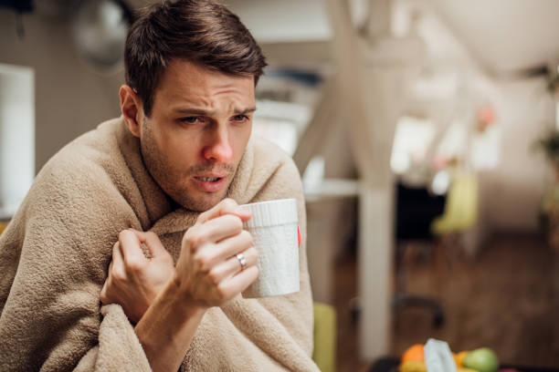 Ill man drinking tea Young man shivering under the blanket and drinking tea cold and flu man stock pictures, royalty-free photos & images