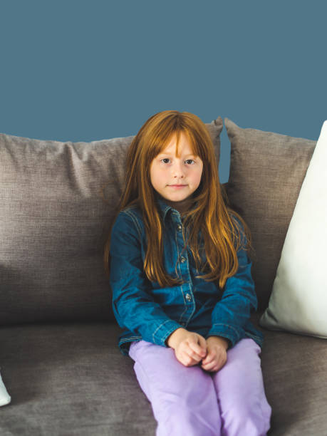istock Redhead little girl looking at us sitting on sofa 1131549559