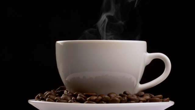 Rotating shot of coffee cup with steam and coffee beans. Slow motion, black background