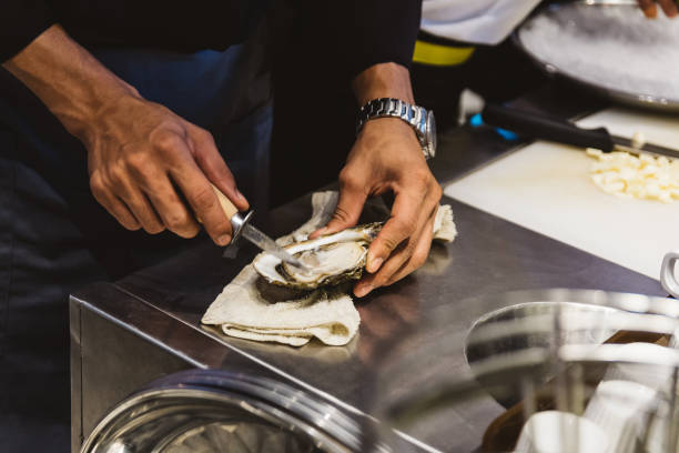 シェフは、ステンレス製のカウンターバーにナイフで新鮮なカキを剥き。 - prepared oysters prepared shellfish shucked seafood ストックフォトと画像