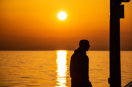 February 20, 2019. Thessaloniki seaside, Greece. Sunset time. Young man silhouette, sun falling over the sea background