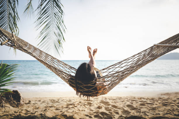 Happy woman relaxing in hammock Summer vacations concept, Happy woman with white bikini, hat and shorts Jeans relaxing in hammock on tropical beach at sunset, Koh mak, Thailand hammock stock pictures, royalty-free photos & images