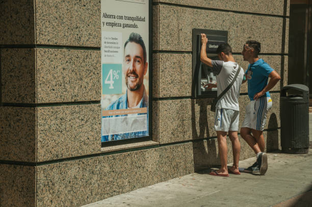 Merida, Spain - July 05, 2018. Young people using a street cash machine in a sunny day at Merida. Founded by ancient Rome in western Spain, the city preserves many buildings of that era.