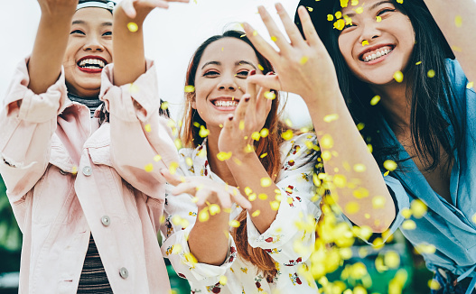 Happy Asian friends having fun throwing confetti outdoor - Young trendy people celebrating at festival event outside - Party, entertainment and youth holidays lifestyle concept