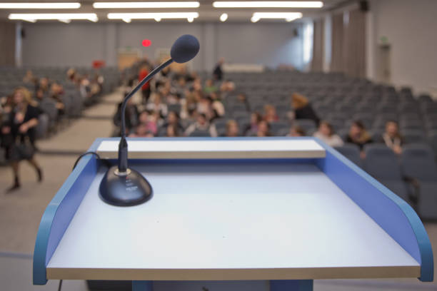 istock Speaker prepare before speaking to the audience behind the podium focused microphone on the podium and blurred empty seat and some of audience . Speech or conference concept. 1131559444
