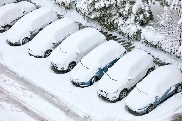 Photo of Cars covered with snow with their windshield wipers lifted in a parking lot in winter