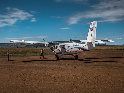 Masai Mara, Kenya - September 6, 2018. The pilots get on a small airplane parked in the savannah flight field on a summer day with the sky full of clouds