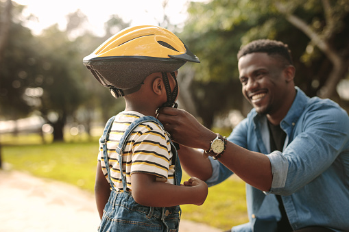 Man helps boy fastens protective helmet for learning to ride bicycle at park. Father helping his son to wear a cycling helmet.