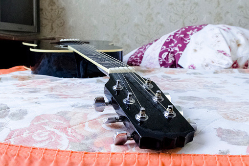 pictured in the photo Acoustic guitar laying on bed low angle shot from bottom with plectrum on the body