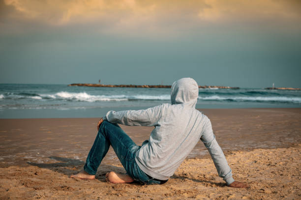 istock Man barefoot sitting on the beach and looking at the sea 1131572834