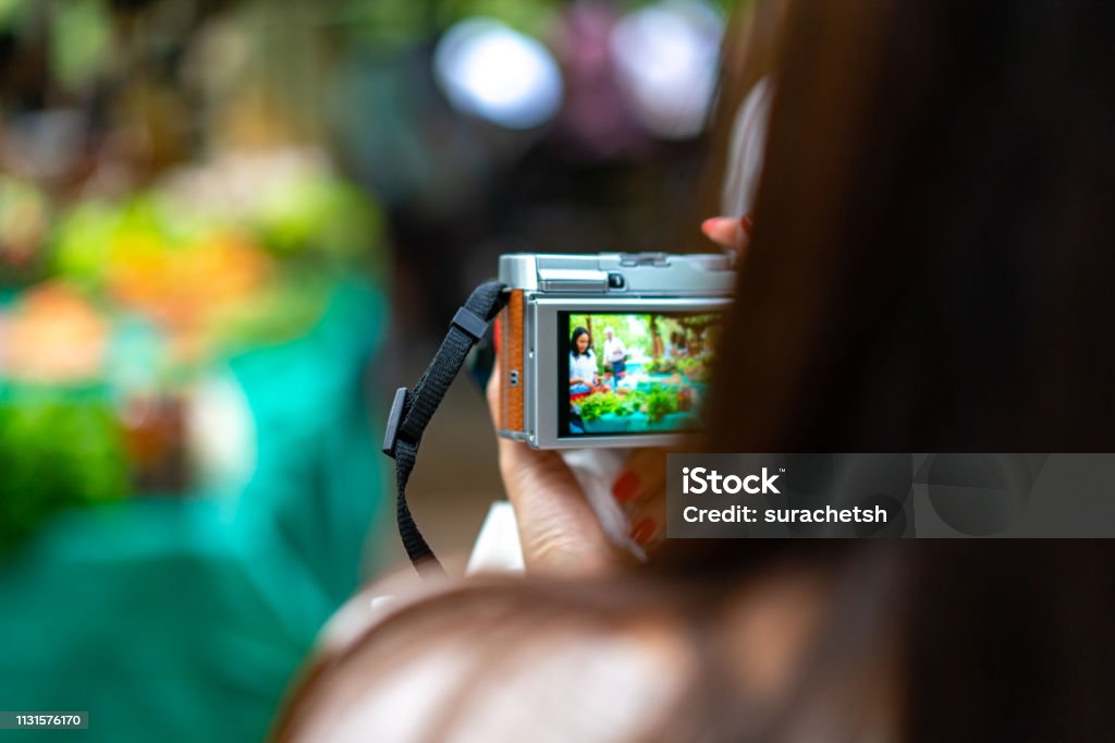 The woman holds the vintage camera, taking a photo of the local vegetable market. Making Stock Photo