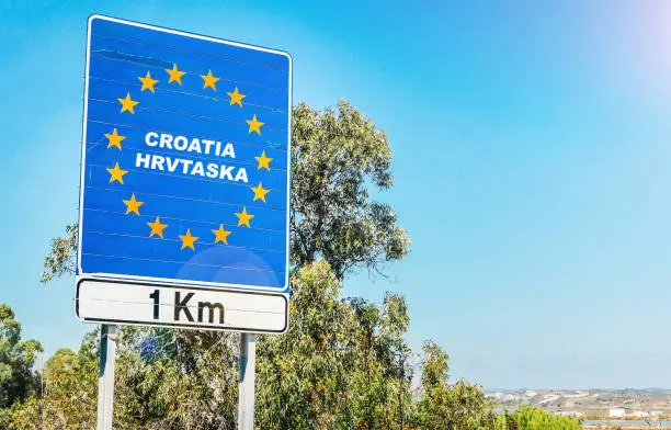 Road sign on the border of a European Union country, Croatia or Hrvatska 1km ahead with blue sky copy space.
