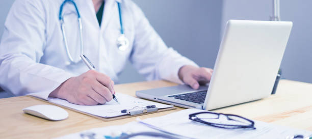 Doctor working in hospital writing a prescription, Healthcare and medical concept,test results in background,Stethoscope with clipboard and Laptop on desk,vintage color,selective focus stock photo