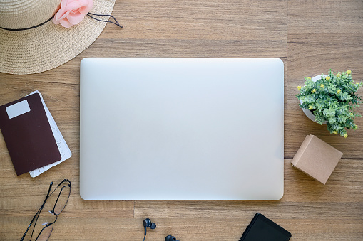 Top view of laptop, passport, hat, glasses and smartphone on wooden table, travel concept.