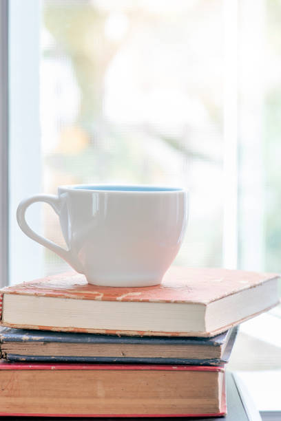 istock white cup on stack of books near the window. 1131579683