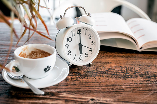 white alarm clock and cup of coffee on wooden table, copy space for text or product display.