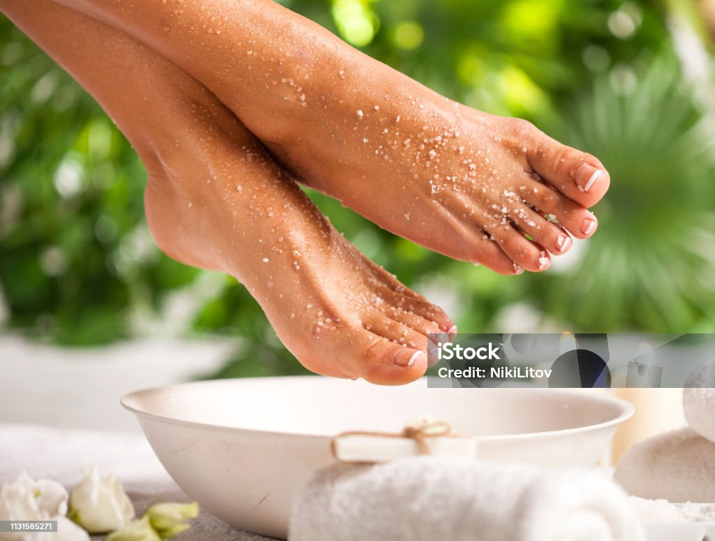 Foot spa on a tropical green leaves background Female feet with sea salt on white floor and tropical green leaves background Foot Stock Photo