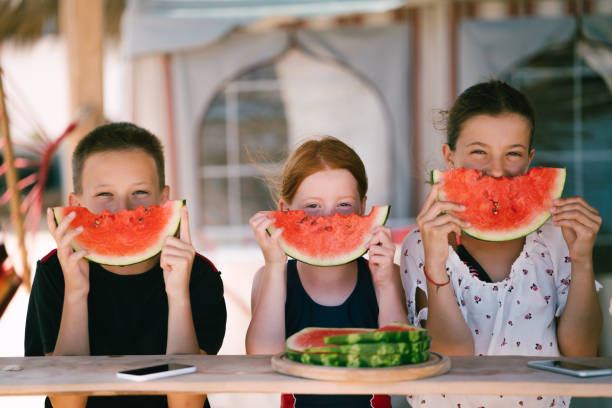 Three kids at the seaside eating sliced watermelon