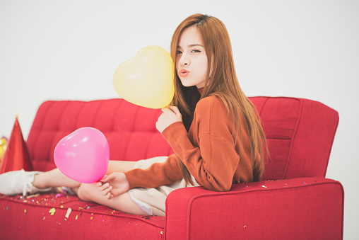 Young beauty Asia woman smiling on a red sofa with hat, balloon white background, New Year party concept
