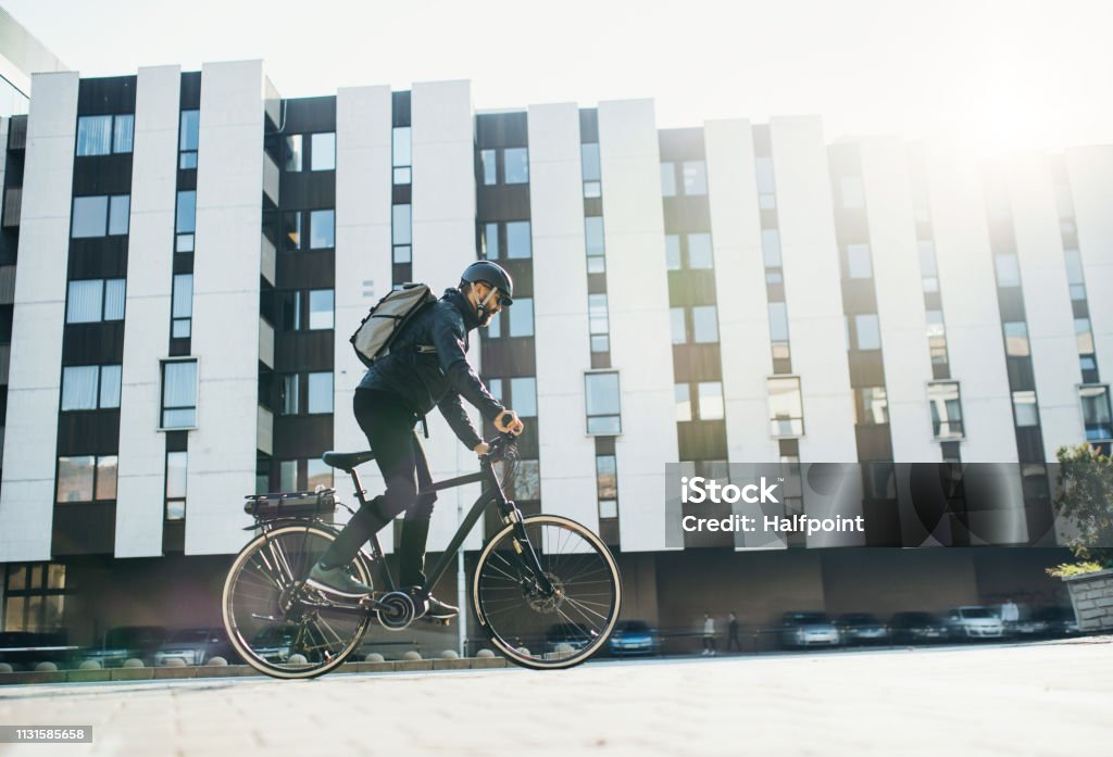 Male courier with bicycle delivering packages in city. Copy space. Male hipster courier with bicycle cycling on a road in city, delivering packages. Copy space. Electric Bicycle Stock Photo