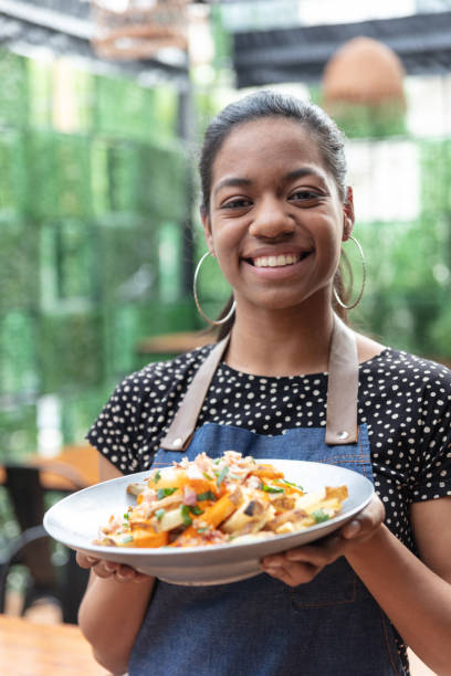 istock Black beautiful waitress at a restaurant holding an order for customer while smiling at camera very cheerfully 1131587078