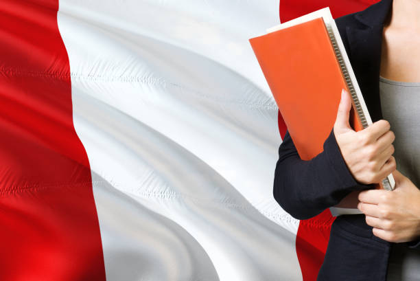 istock Learning Peruvian language concept. Young woman standing with the Peru flag in the background. Teacher holding books, orange blank book cover. 1131591668