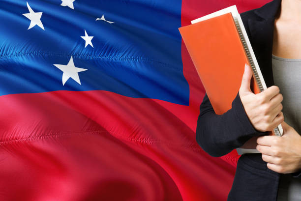 istock Learning Samoan language concept. Young woman standing with the Samoa flag in the background. Teacher holding books, orange blank book cover. 1131591683
