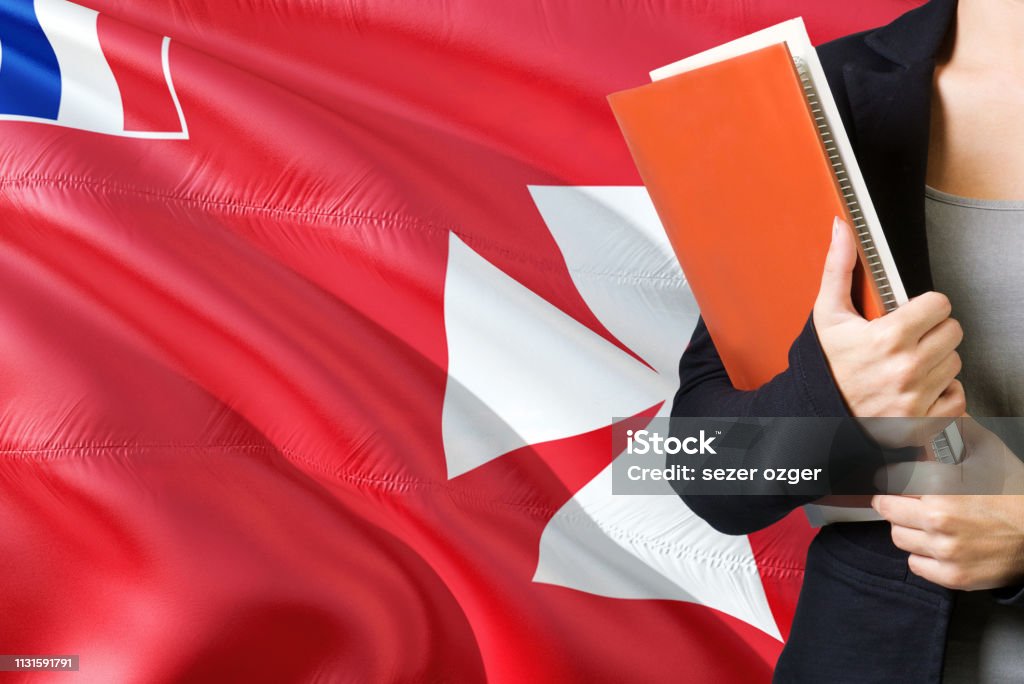 Learning language concept. Young woman standing with the Wallis And Futuna flag in the background. Teacher holding books, orange blank book cover. Adult Stock Photo