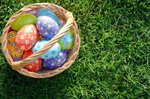 Photo of Flat lay shot of Easter eggs in the wicker basket on green spring grass. Space for text