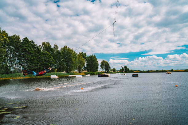 Young man wakeboarding on a lake Marupe, Latvia - November 15, 2017: Young man wakeboarding on a lake, making raley, frontroll and jumping the kickers and sliders. Wakeboard. kiteboarding stock pictures, royalty-free photos & images