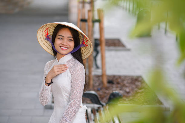 Close up portrait of pretty asian girl dressed in Ao Dai dress wearing vietnamese conical hat. Close up portrait of pretty asian girl dressed in national traditional Ao Dai dress with vietnamese conical hat against arches background. ao dai stock pictures, royalty-free photos & images