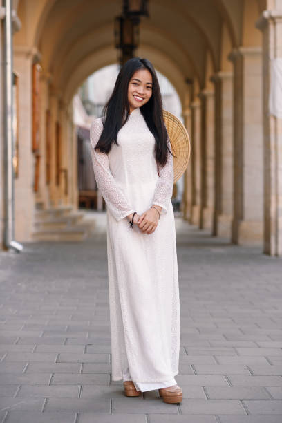 Beautiful happy asian girl dressed in Ao Dai dress with vietnamese conical hat against arches background. Beautiful happy asian girl dressed in national traditional Ao Dai dress with vietnamese conical hat against arches background. ao dai stock pictures, royalty-free photos & images