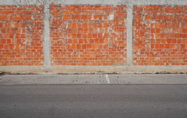 istock Wall made with different types of bricks and strips of cement. Sidewalk and asphalt road in front. Urban  background for copy text 1131605892