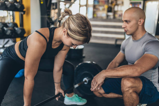istock Woman exercise with barbell with her trainer 1131606756
