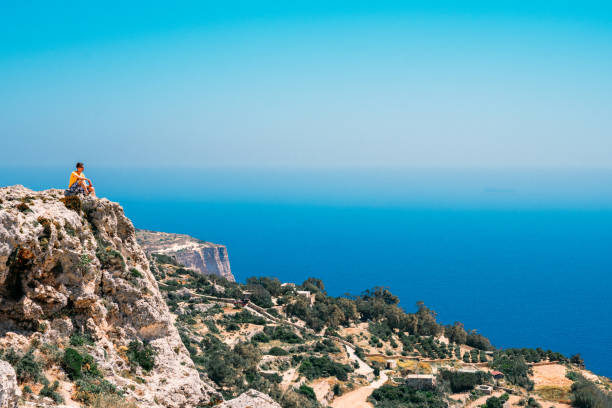 young man sitting on the edge of the cliff - climbing men sea cliff imagens e fotografias de stock