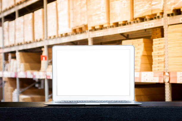 istock Mock up of modern computer or laptop with blank screen on table with Blurred boxes on rows of shelves in warehouse. 1131610650