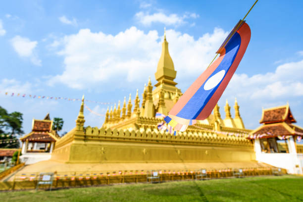 (selective focus) Some Laos flags waving in the foreground with the blurred Pha That Luang in the background.  Pha That Luang is a gold-covered large Buddhist stupa in the centre of the city of Vientiane, Laos.