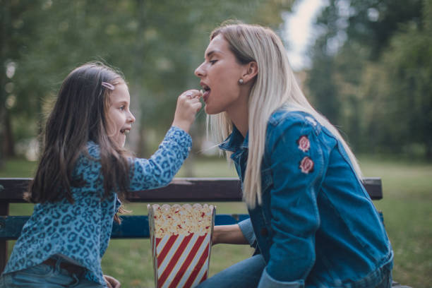 istock Mother and daughther eating popcorn in park 1131615392