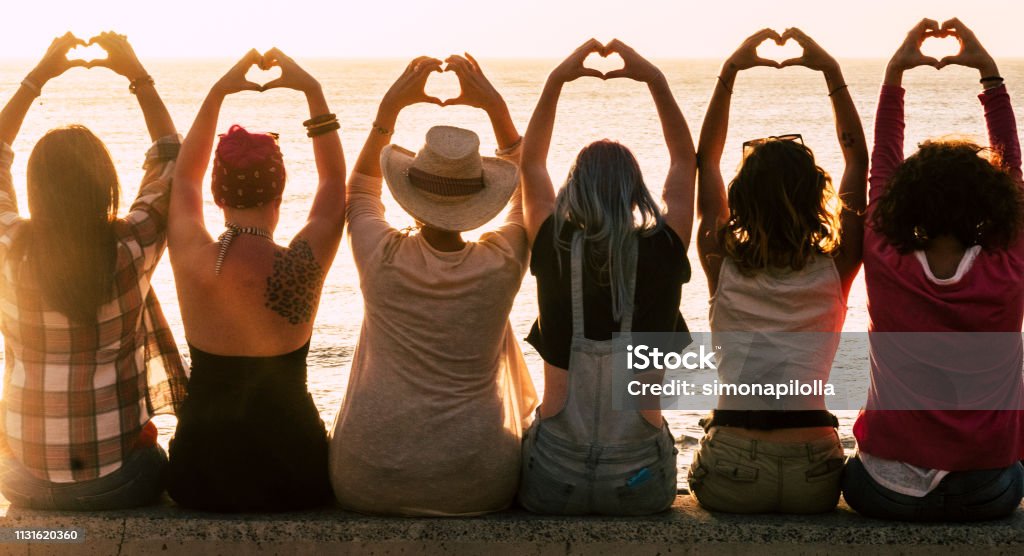 Love and meditation lifestyle concept - group of women looking at the sunset on the ocean and make the hearth with hands - romantic golden light and valentine's day concept - friendship forever Women Stock Photo