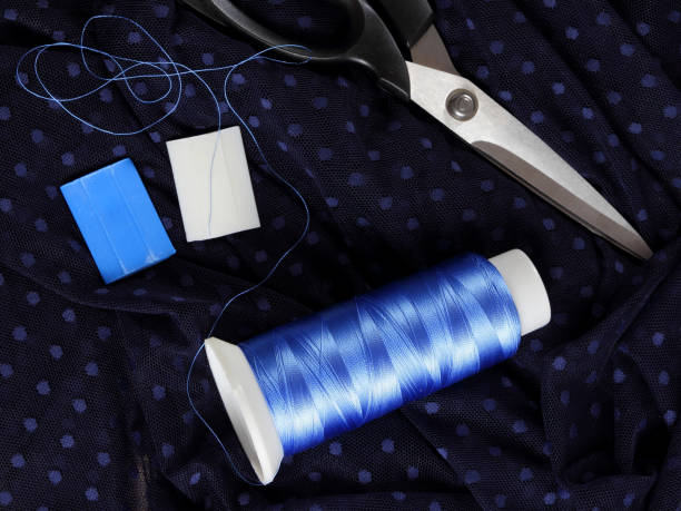 istock Dark fabric with polka dots and blue silk thread. Process of tailoring. Scissors and bobbin of thread on black fabric. Brilliant blue threads for sewing. Top view 1131620959