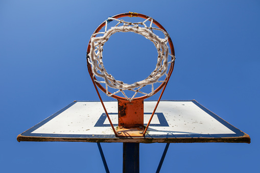 Old and damaged basketball hoop and net seen from below. Sunny day with blue sky.