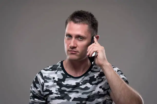 Portrait of confident but annoyed displeased young adult man talking on the mobile phone looking at camera