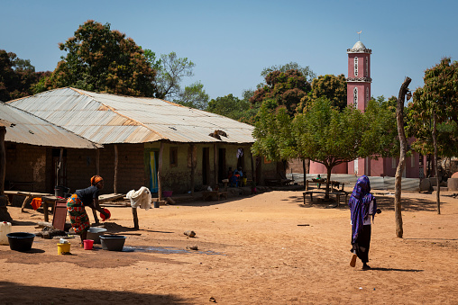 Gabu Region, Republic of Guinea-Bissau - February 7, 2018: People at the village of Mandina Mandinga in the Gabu Region with a mosque on the background, in Guinea Bissau.