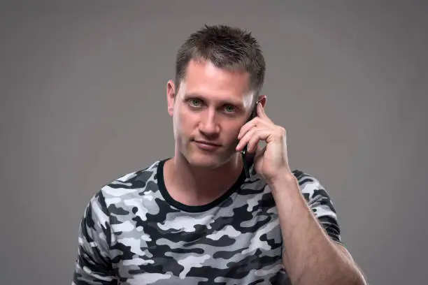 Portrait of handsome young adult man talking on the mobile phone and smiling looking at camera over gray background.