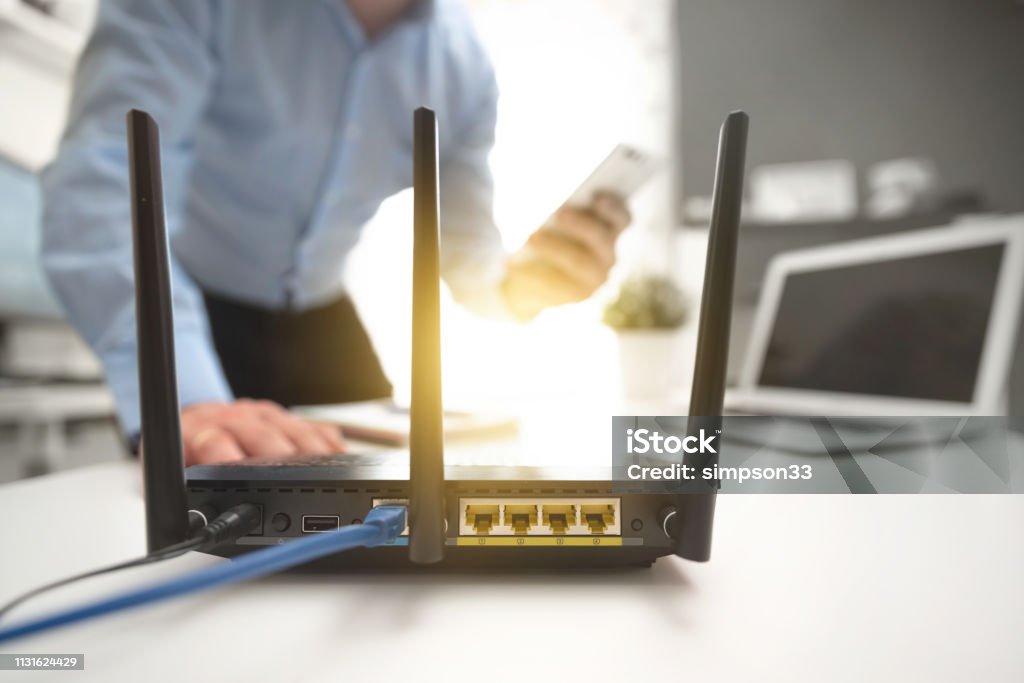 Wireless router concept. Man using smartphone Wireless router with three antennas and cable connected. Man using smartphone in background Router Stock Photo