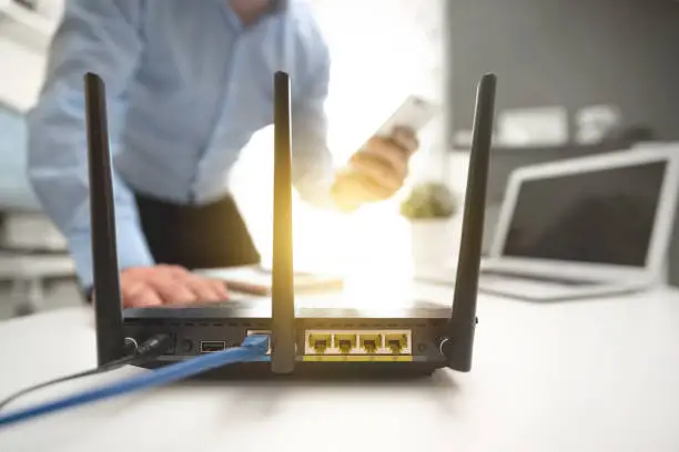 Wireless router with three antennas and cable connected. Man using smartphone in background