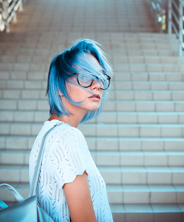 Close-up portrait of a hipster girl wearing glasses with blue hair. Atypical beauty. Street fashion.