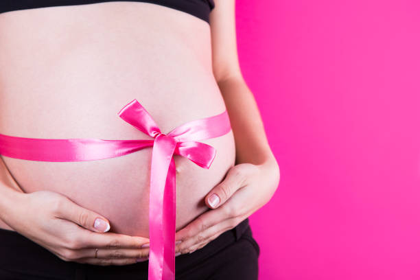 Close-up belly of pregnant woman with satin ribbon tied around it in the form of bow as gift on pink background. Close-up belly of pregnant woman with satin ribbon tied around it in the form of bow as gift on pink background. It's a Girl. Baby Shower concept with copy space, studio shot. cute pregnant woman with gift stock pictures, royalty-free photos & images