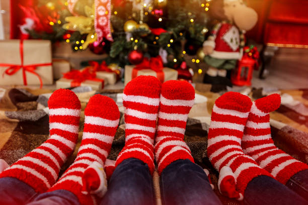 Warm socks in red and white stripes on the background of the Christmas tree Warm socks in red and white stripes on the background of the Christmas tree heat home interior comfortable human foot stock pictures, royalty-free photos & images