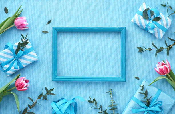 istock Blue background with wrapped gift boxes and eucalyptus twigs around empty wooden frame 1131654203